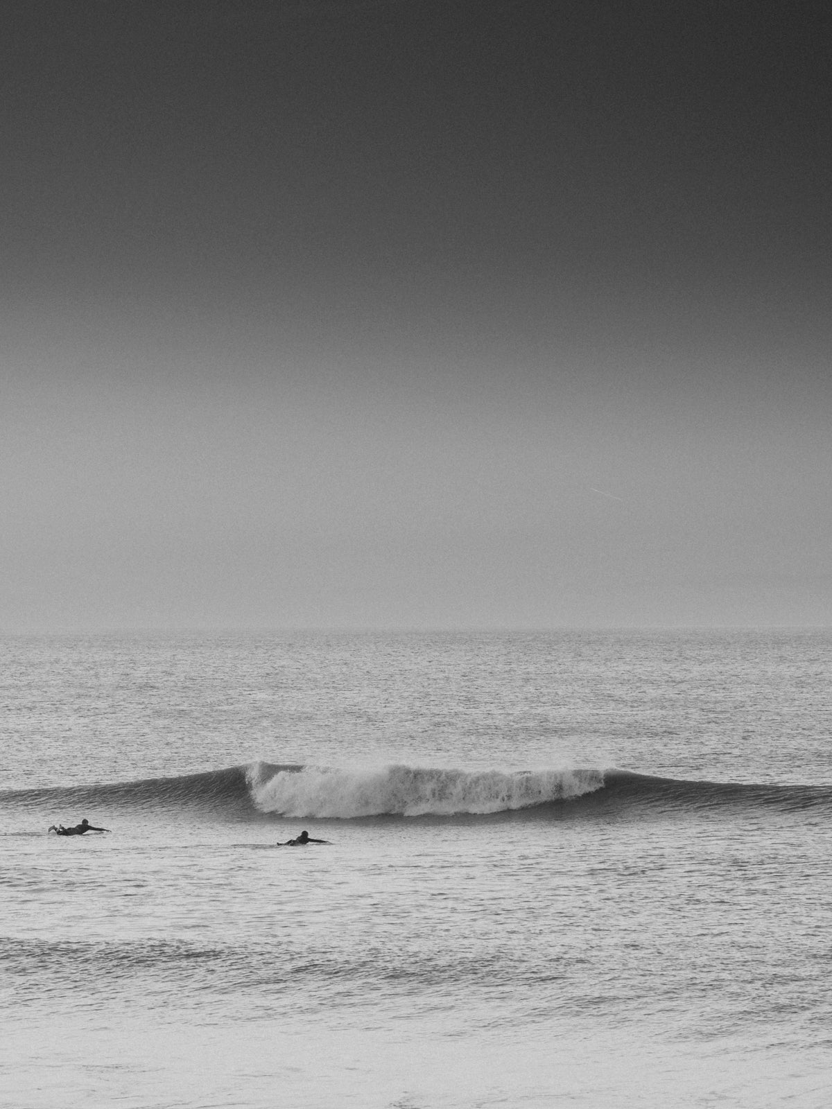 Two surfers paddle in a serene landscape. Black and white photography on the Dutch coast.