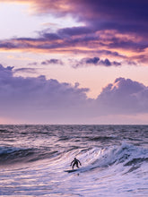 Load image into Gallery viewer, One surfer is surfing a wave in The Netherlands with a bright purple sky and purple glow on the north sea surface.
