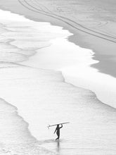 Load image into Gallery viewer, a black and white photograph of a woman in silhouette carries a surfboard on her head through the shoreline of a dutch beach.
