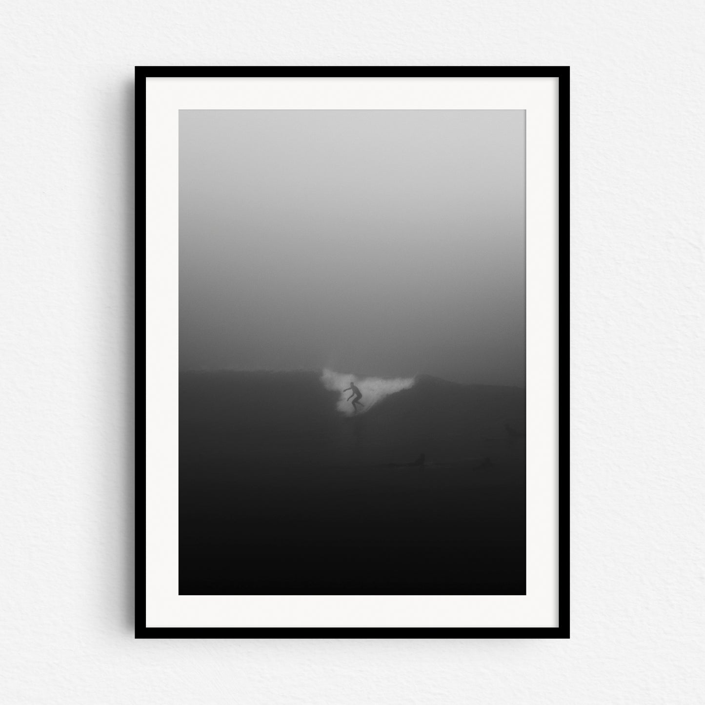 A surfer riding a wave in thick fog in the North Sea. Framed in black wood for stylish surf art from The Hague.