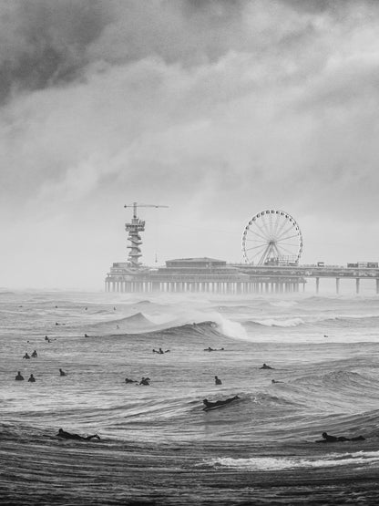 Surfers in a moody black adn white scene in front of the iconic Scheveningen pier.