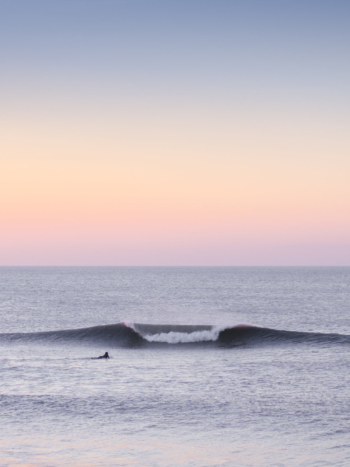 Surfer in a pastel coloured evening sky with a big wave, captured by Jop Hermans.