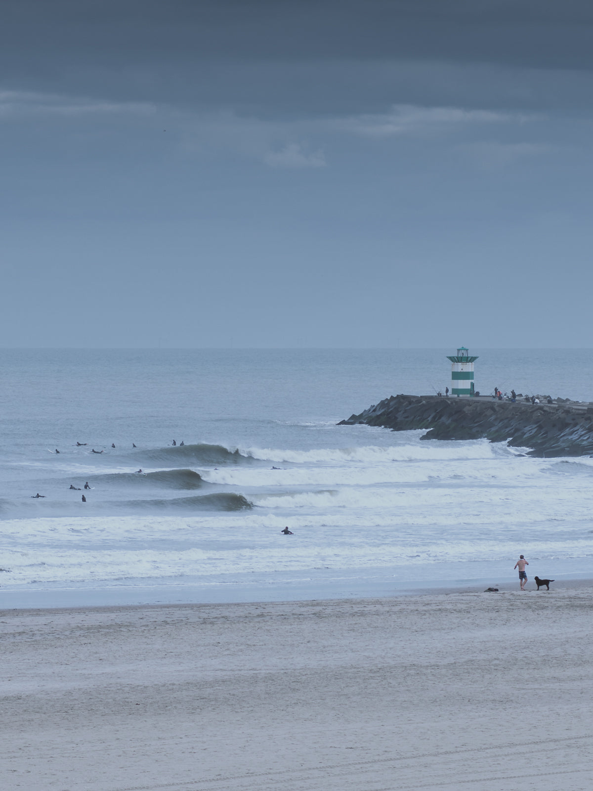 Big waves break next to the lighthouse in The Hague. A moody winter surf print, captured by Jop Hermans.