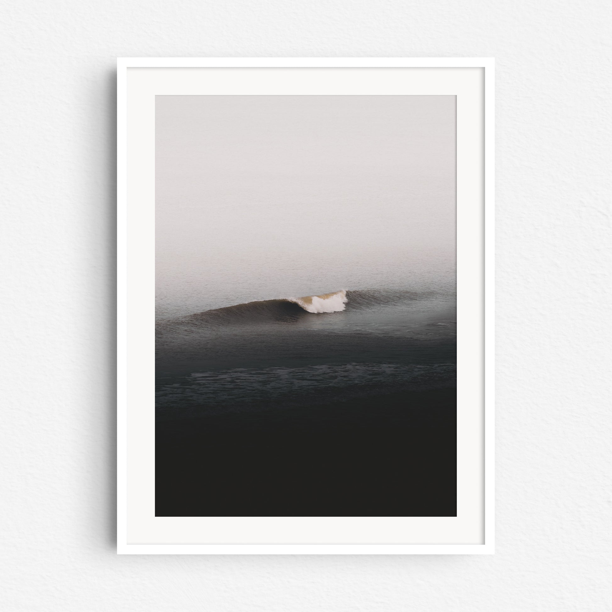 The photo of a clean wave breaking in the Dutch North Sea, in a white wooden frame.