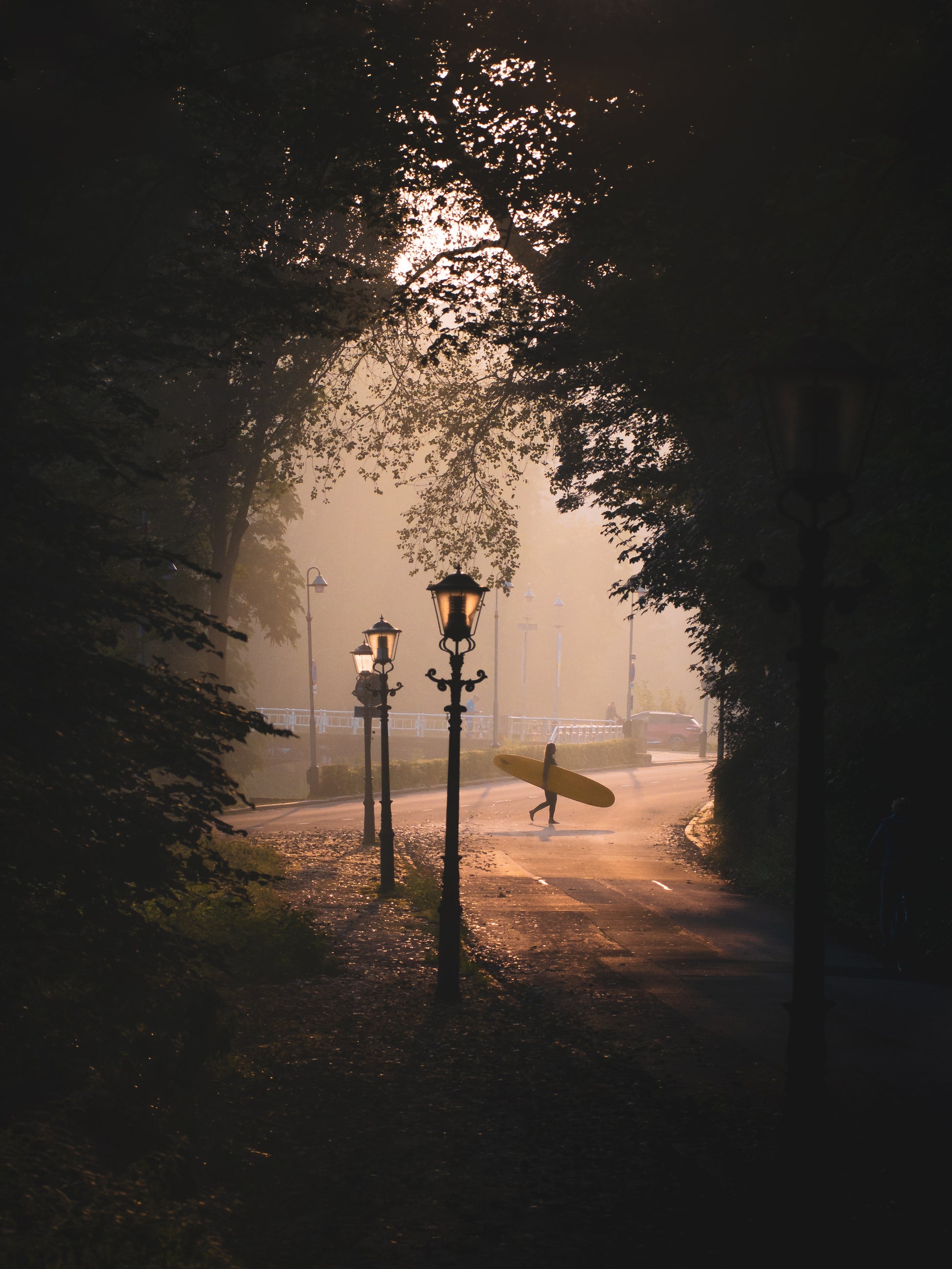 A surfer crosses the road in Scheveningen, carrying a longboard in a misty landscape while the sun was rising.