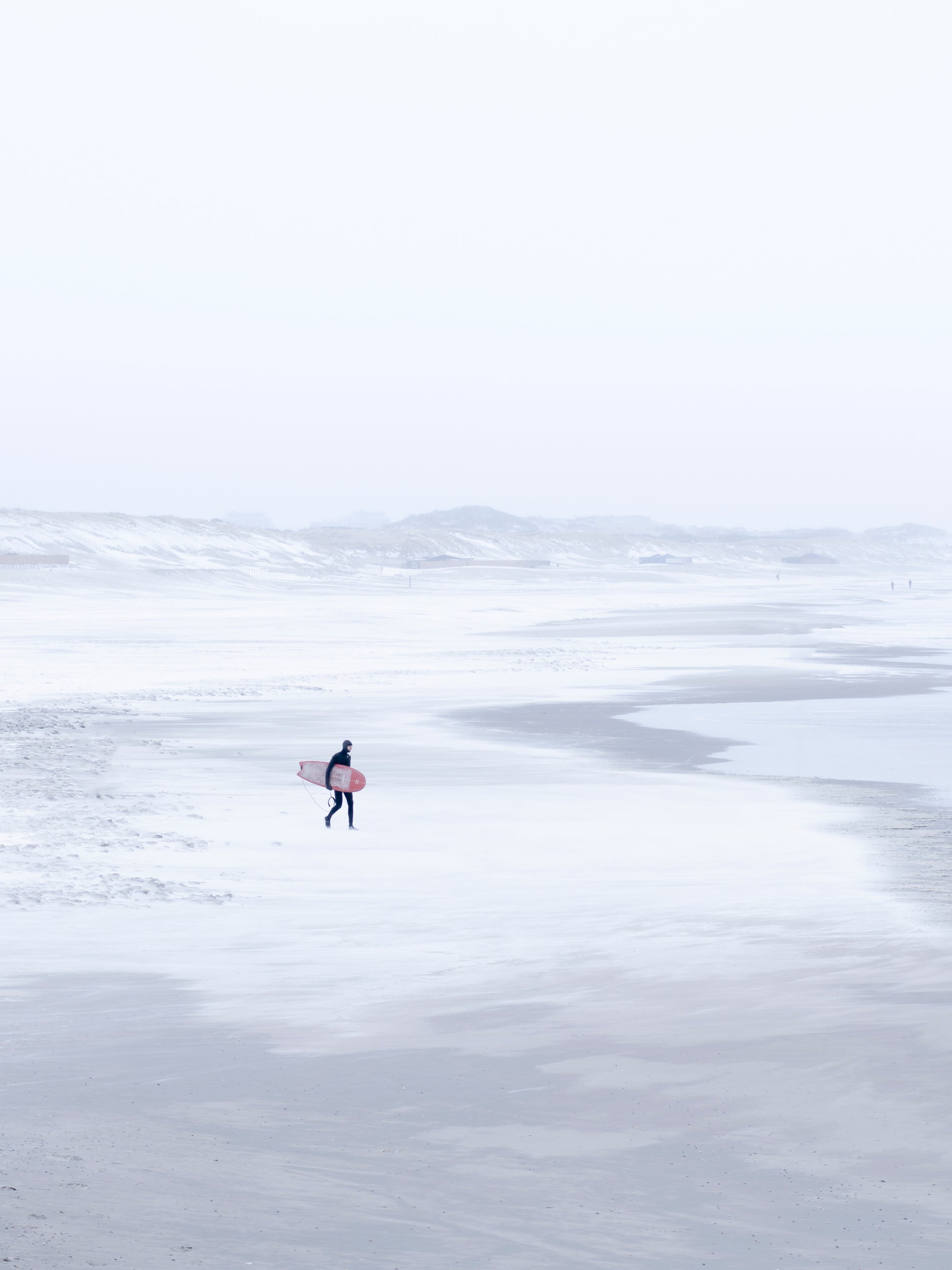 Winter surf photography in Scheveningen where a surfer walks over the snowy beach.