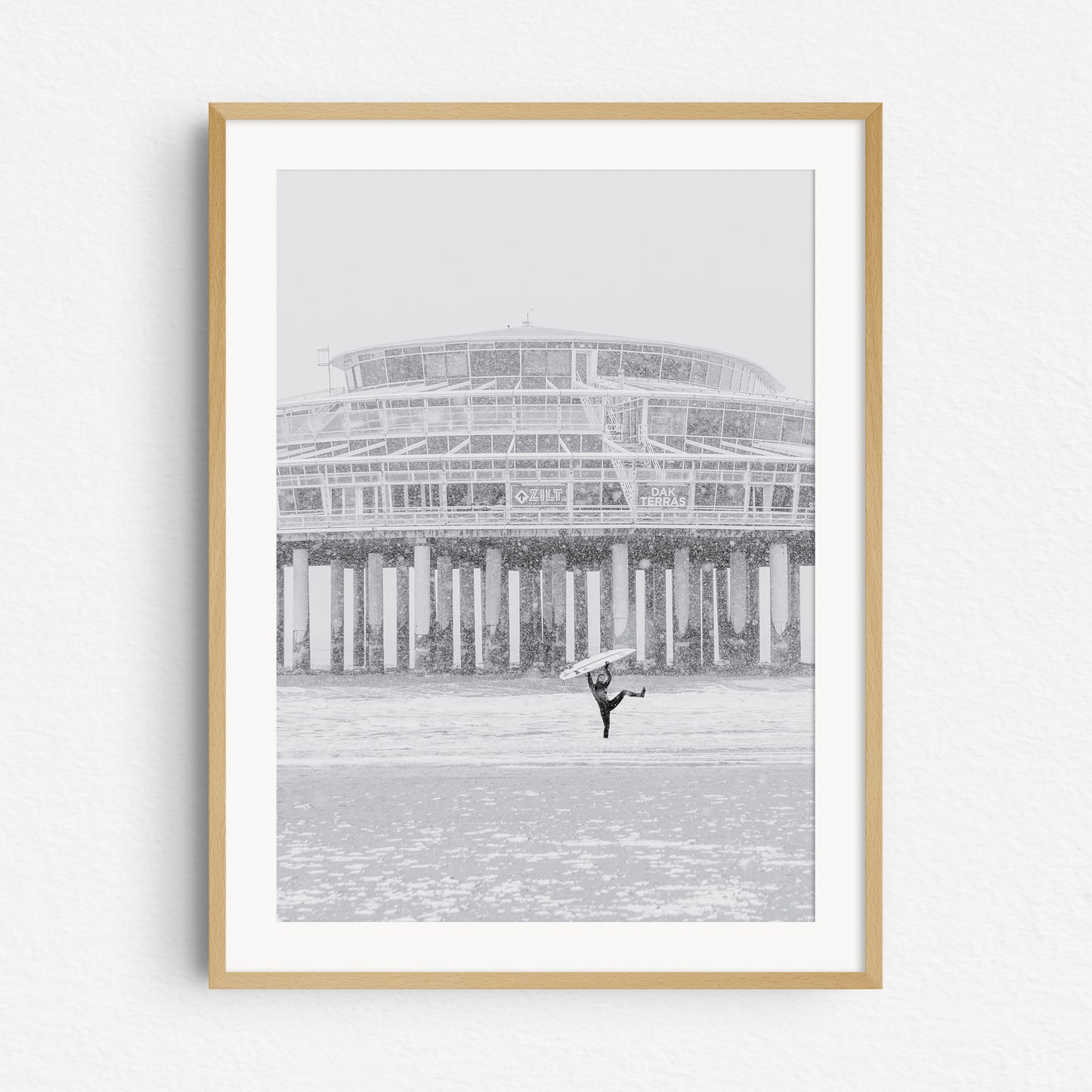 A local The Hague surfer is happy during a surf session in a snow storm, framed in a natural wooden frame.