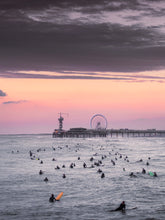 Load image into Gallery viewer, Many surfers in the water during sunset near the iconic Scheveningen pier. Art prints from The Hague.
