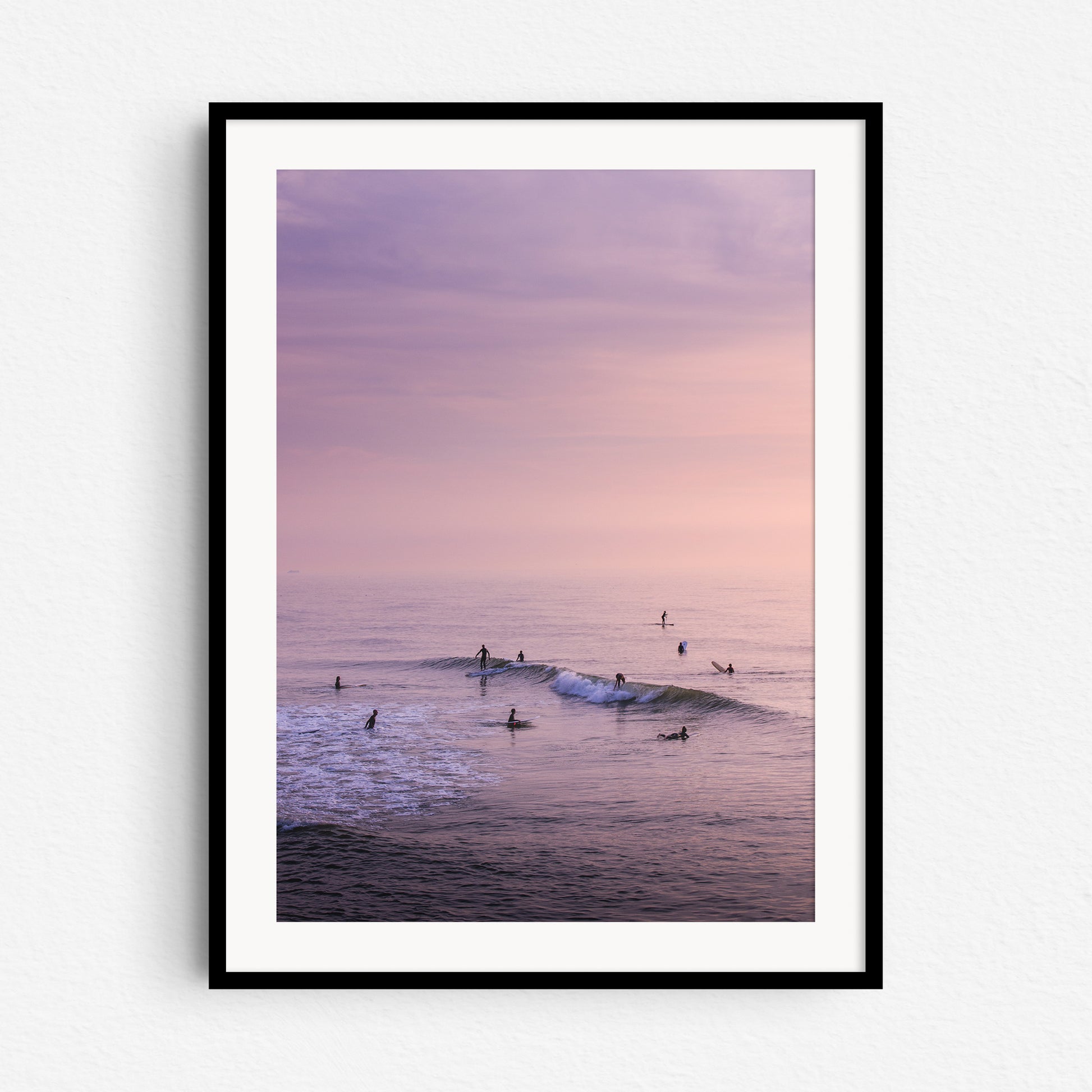 Surfers during a summer sunset in a colourful sea, in a black wooden frame.