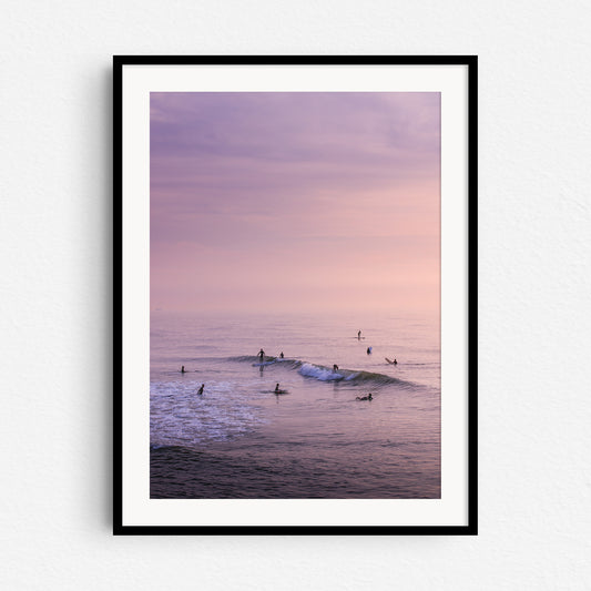 Surfers during a summer sunset in a colourful sea, in a black wooden frame.