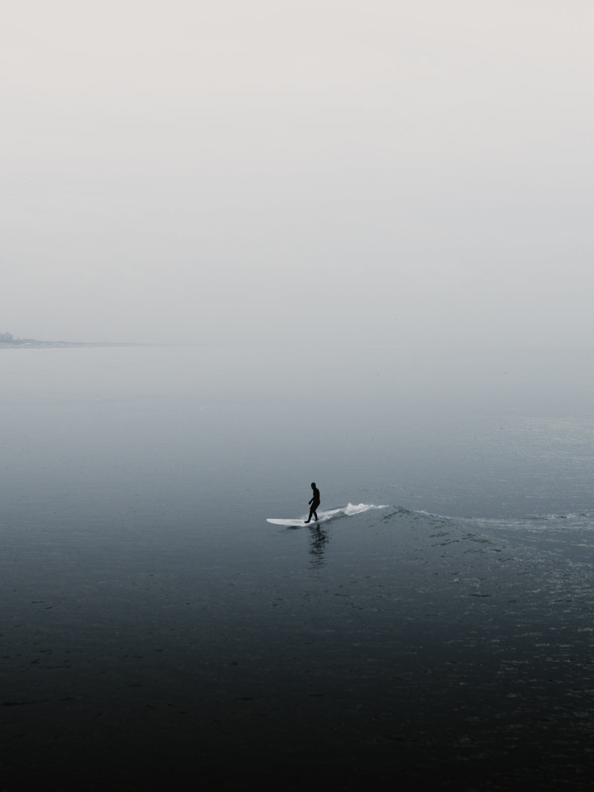 A peaceful silhouette of a surfer in Scheveningen. The landscape foggy with a shallow depth of field. Perfect for adding calming wall art with sea and surf to your space. Captured by Jop Hermans