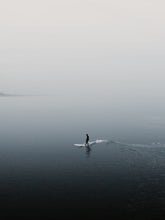 Load image into Gallery viewer, A peaceful silhouette of a surfer in Scheveningen. The landscape foggy with a shallow depth of field. Perfect for adding calming wall art with sea and surf to your space. Captured by Jop Hermans
