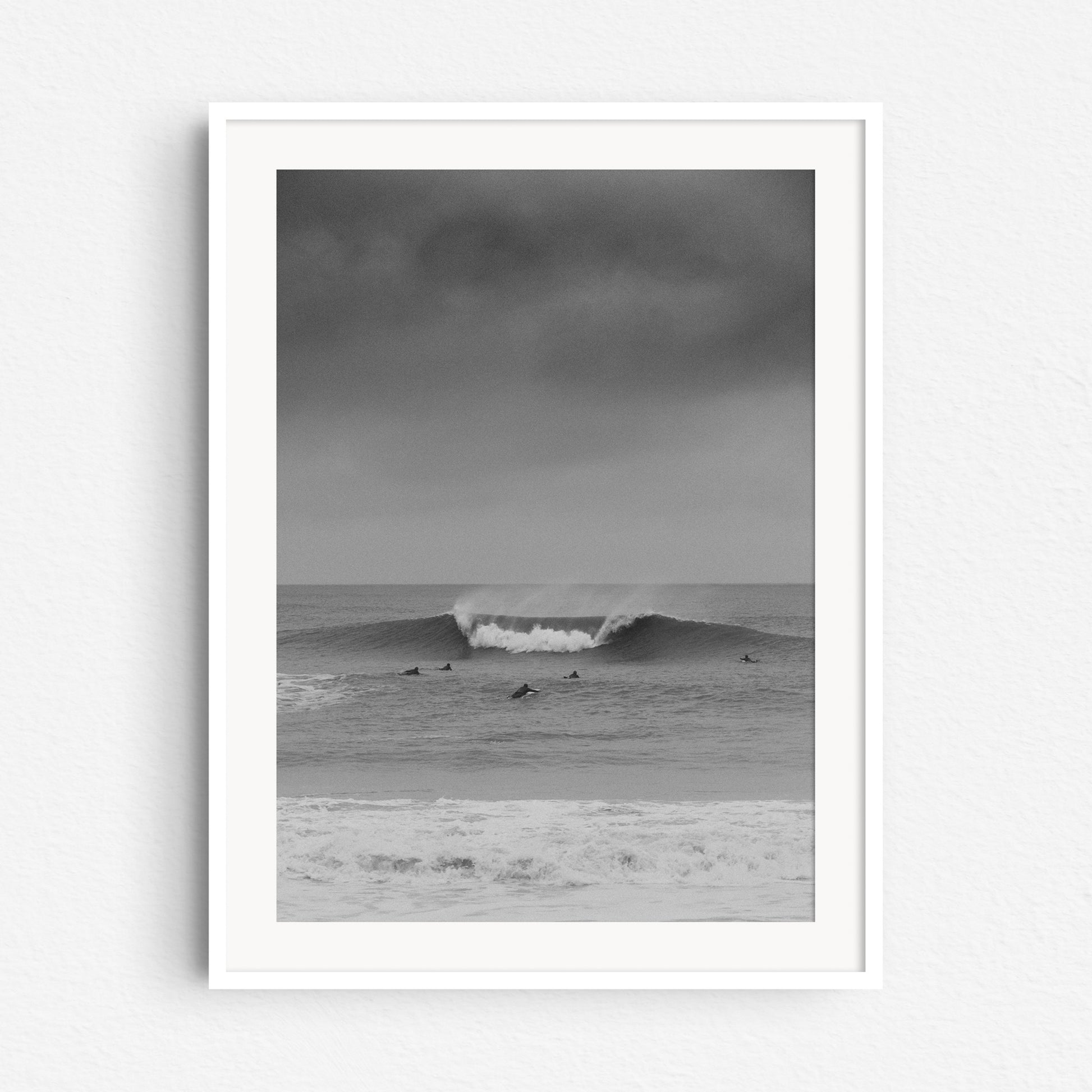 A framed surf photograph of surfers in the Netherlands paddling towards a large wave, captured by Jop Hermans.