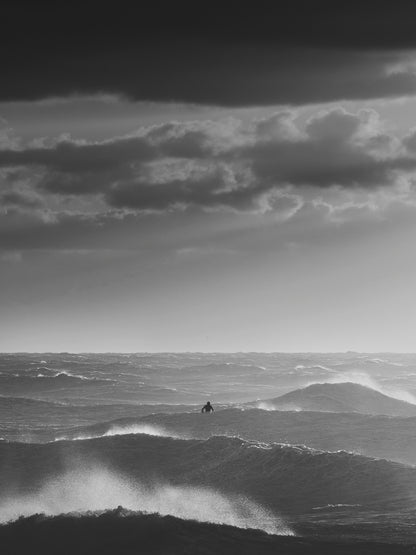 A surfer silhouette sits in between heavy waves in the North Sea.