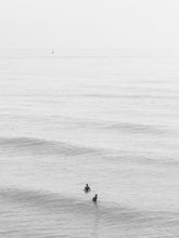 Load image into Gallery viewer, Minimal black and white photography of surfers in the North Sea, available as photo print.
