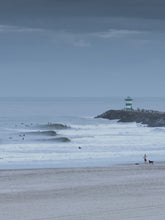 Load image into Gallery viewer, Surfers in the water next to amazing waves. The photo has a blue hue which gives it a moody feel.
