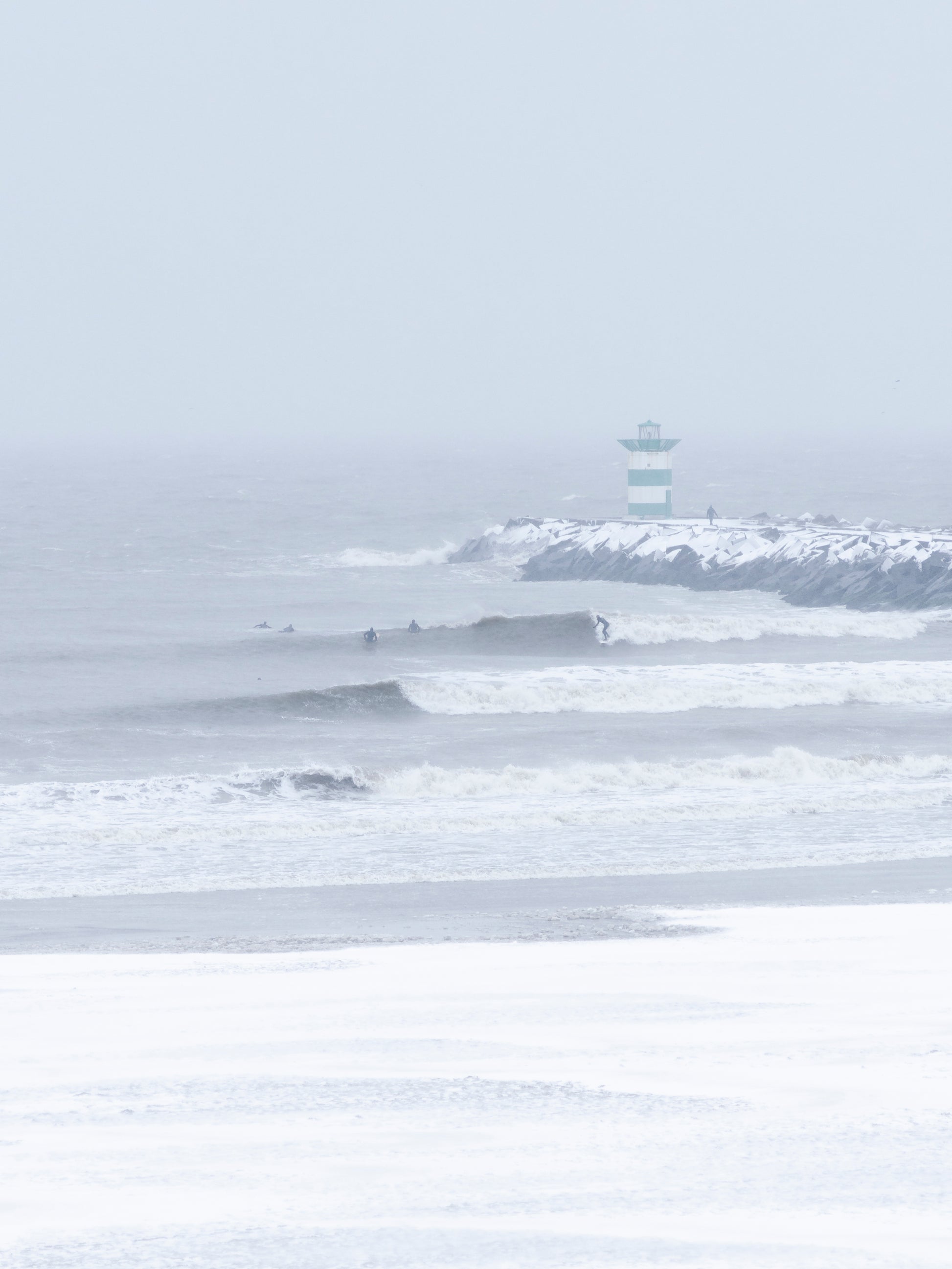 Big waves being surfed in a snowstorm in The Netherlands. Available as print, captured by Jop Hermans.