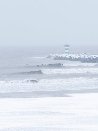 Big waves being surfed in a snowstorm in The Netherlands. Available as print, captured by Jop Hermans.