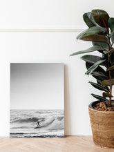 Load image into Gallery viewer, Black and white photo print standing on a wooden floor next to a green plant.
