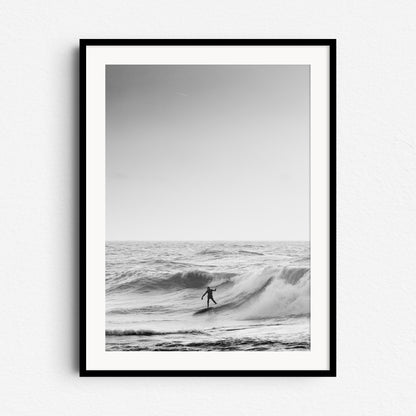 Black and white photo of a surfer riding a wave in the North Sea, framed in black wood, perfect as large wall decoration for photo art lovers.