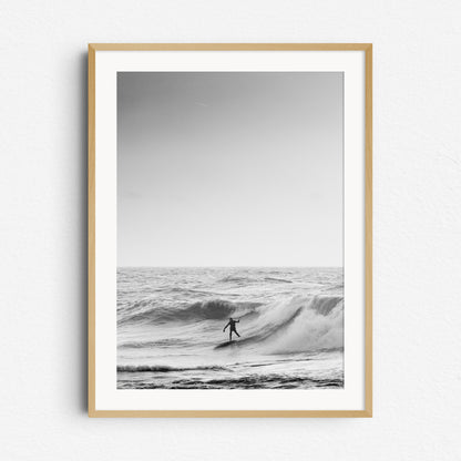 The silhouette of a North Sea surfer slides down a big wave in black and white, framed in natural wood, a great choice for elegant wall decoration.