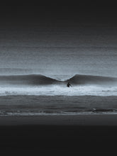 Load image into Gallery viewer, Black and white photograph of a wave breaking right in front of a surfer walking towards the wave in Scheveningen - The Hague.
