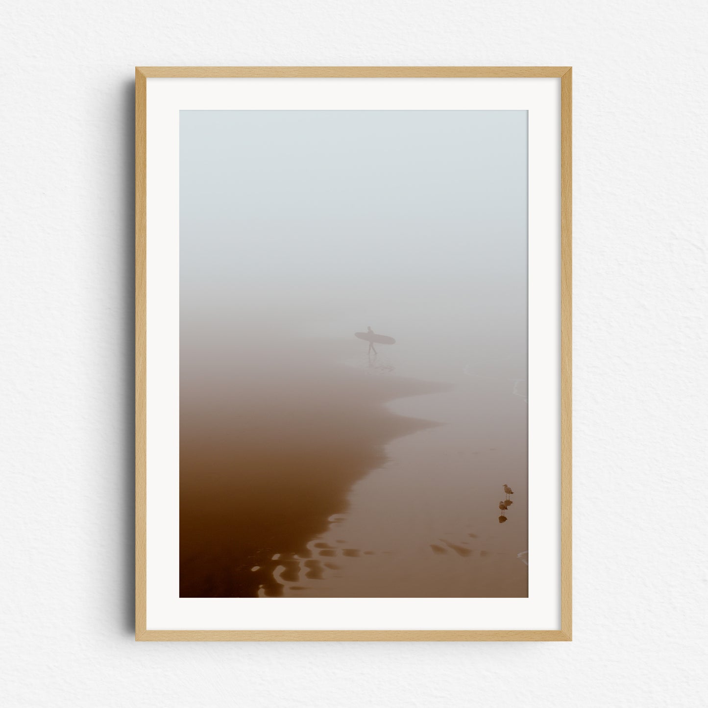 Print in natural wooden frame: Serene beach scene with a surfer leaving the water, framed in natural wood to enhance the calming aesthetic.