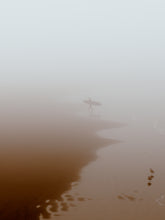 Load image into Gallery viewer, Quiet beach with a surfer leaving the water, capturing a peaceful moment in thick fog. Perfect for wall art.
