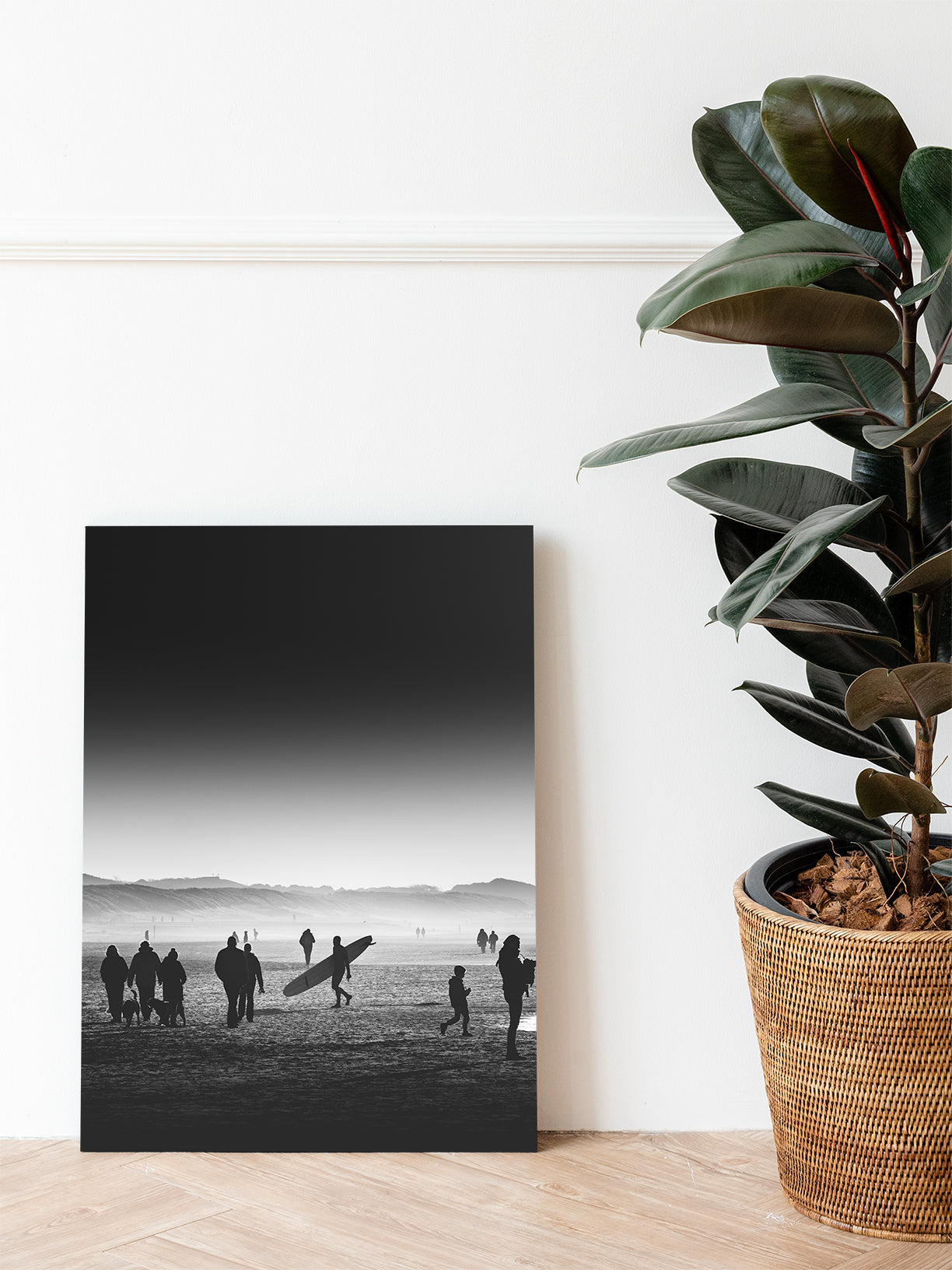 Black and white surf photo art from The Hague. A monochrome photo of a surfer with a longboard walking back from sea and surf. Printed on aluminium dibond with the print leaning against a livingroom wall.