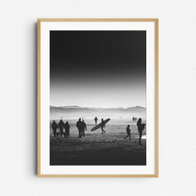 Load image into Gallery viewer, Surfer walking with a longboard on a misty Scheveningen beach in black and white. Dunes in the background. Framed in natural wood, adding a timeless touch to North Sea Surf Photos.
