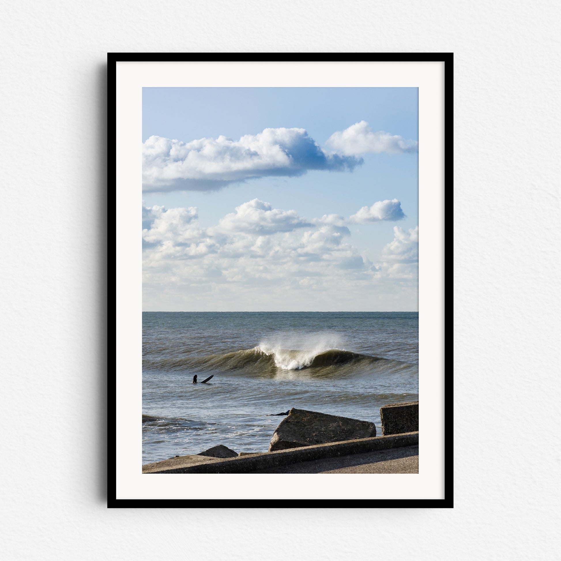 Surfing near the Scheveningen harbor wall on the Zuiderstrand. Blue skies and white clouds. Framed in black wood for a striking and dynamic surf scene.