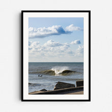 Load image into Gallery viewer, Surfing near the Scheveningen harbor wall on the Zuiderstrand. Blue skies and white clouds. Framed in black wood for a striking and dynamic surf scene.
