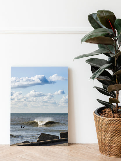 Mockup of a dibond photo print of a Dutch seascape standing next to a green plant. Surf and Sea photography from The Netherlands.