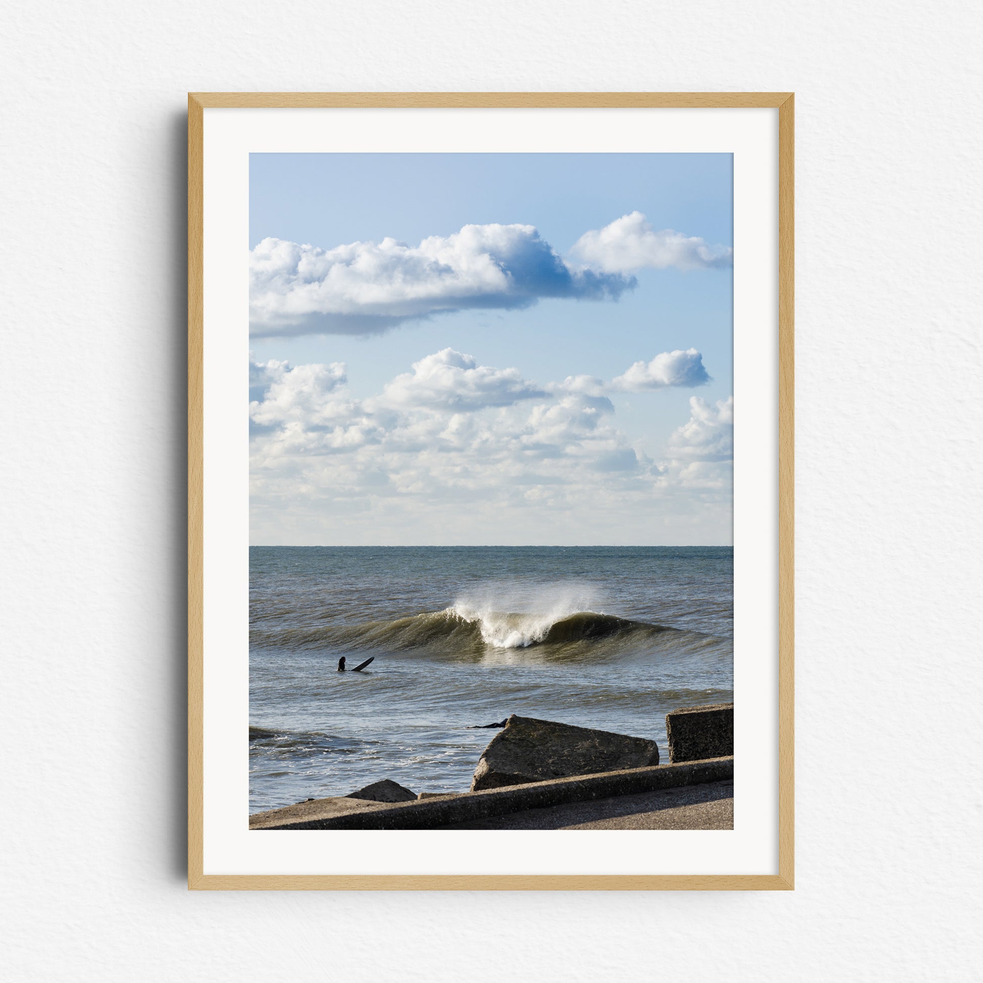 A surfer in The Netherlands near the harbor wall in front of a large breaking wave, framed in natural wood for a relaxed, coastal vibe.