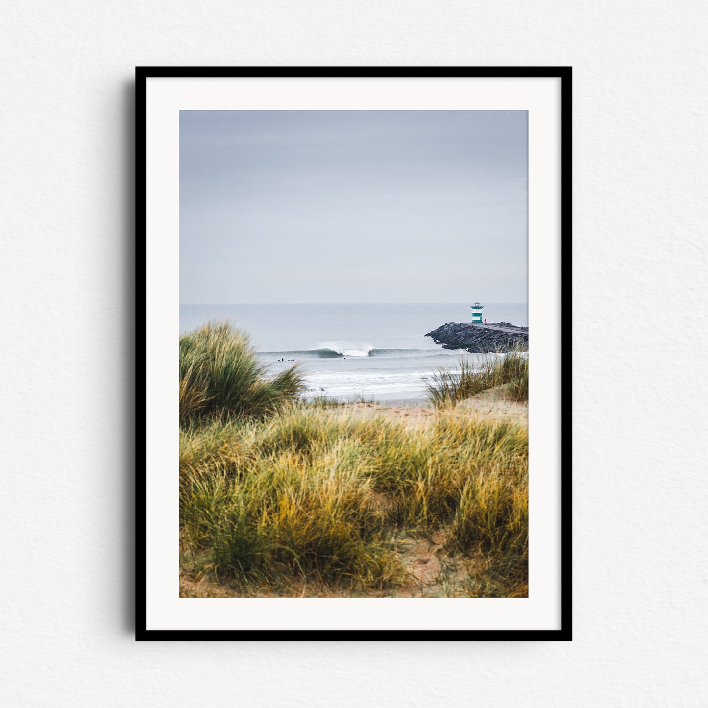 Contrasting colours on the Scheveningen coast. Dunes in the foreground and a large wave breaking near the horizon. Dutch artwork framed in black wood for a striking display.