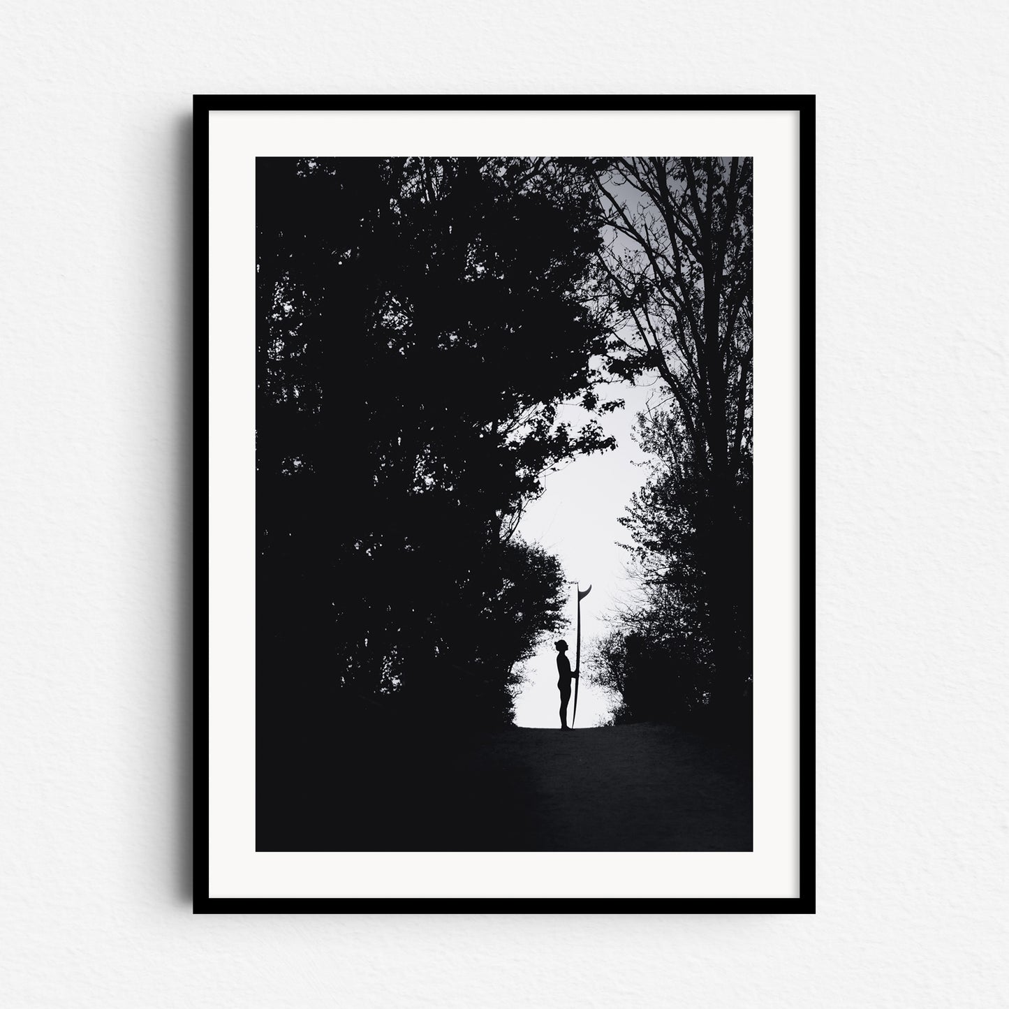 Black and white silhouette of a female surfer holding a longboard in a forest in The Hague, framed in black wood, ideal for Dutch photo art enthusiasts.