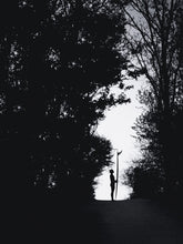 Afbeelding in Gallery-weergave laden, At the end of a forest path you see the silhouette of a girl holding a surfboard with the fin visible. Black and white photography printed on aluminium dibond. Surf artwork from The Hague.
