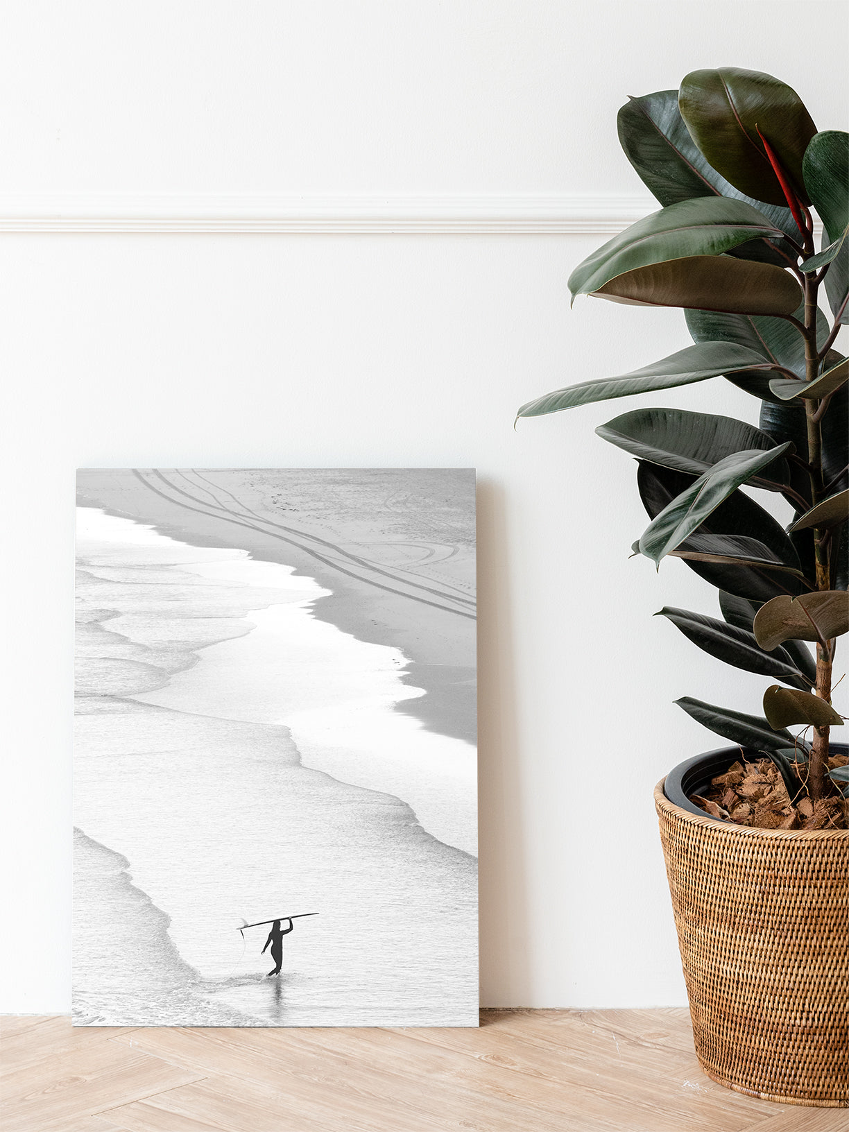 Dibond print of black and white surf photography from The Netherlands, placed on a livingroom floor next to a green plant. 