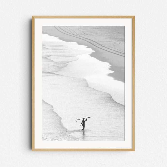 Peaceful black and white image of a surfer walking on the beach in The Hague, framed in natural wood for a warm, organic look. 