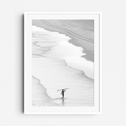 Serene surf photo with a woman carrying her longboard, framed in white wood to enhance the tranquil, minimalist vibe. Captured bij Jop Hermans