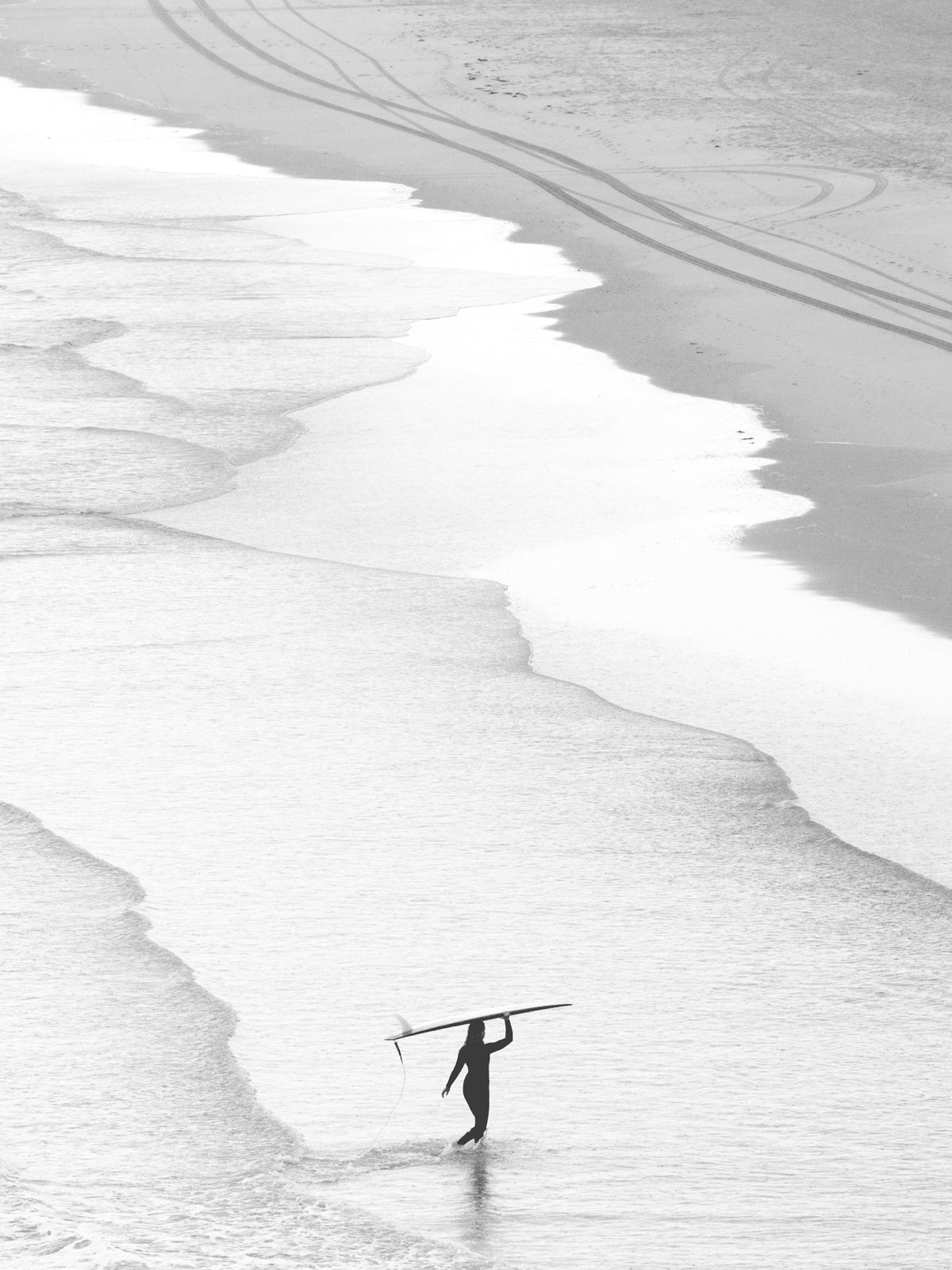 Black and white photo of a surfer carrying her longboard, capturing solitude and nature’s calm, ideal for surf art lovers. Captured in The Hague by Jop Hermans