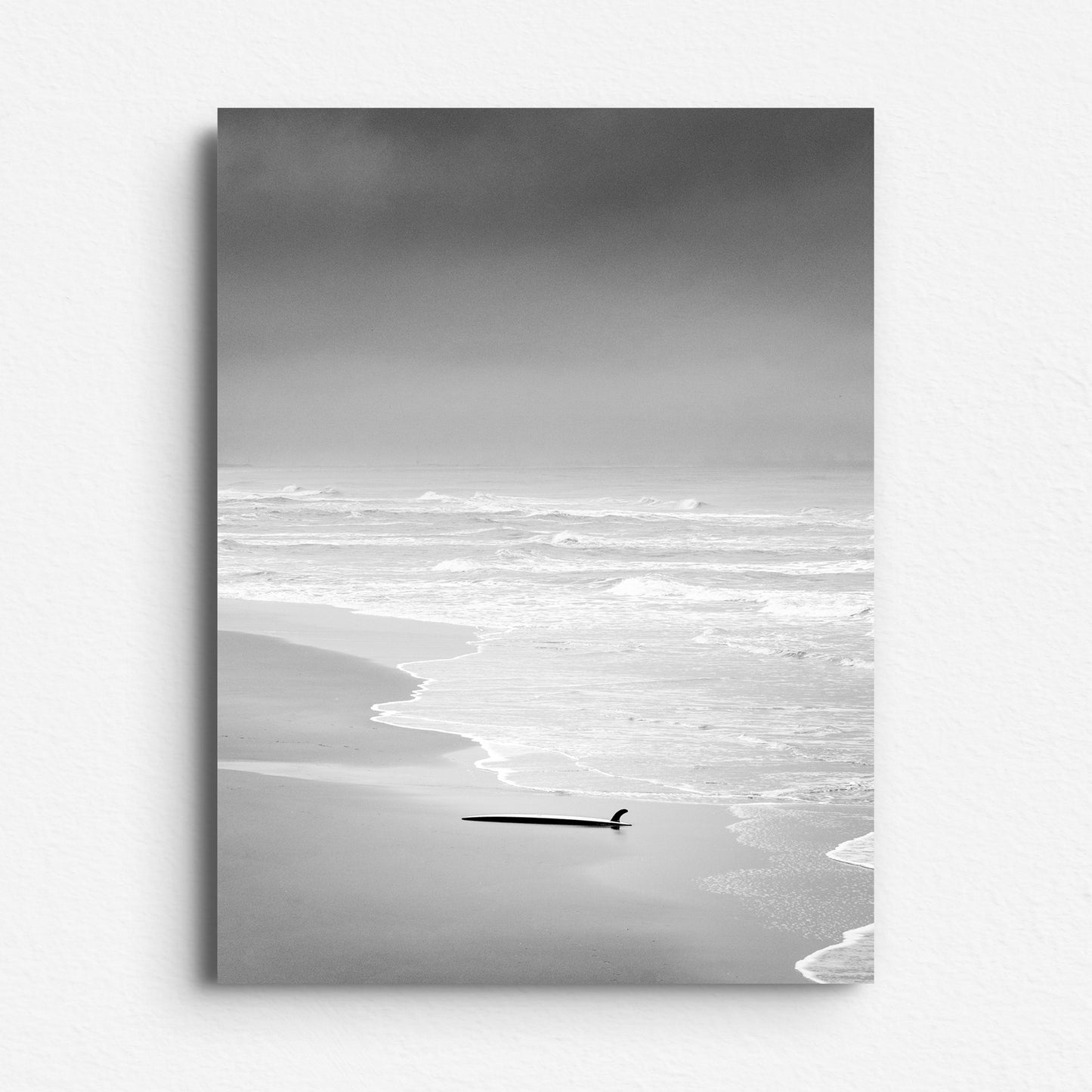 Black and white photo of a surfboard on a quiet beach, printed on Dibond for a sleek and minimalist Photo Poster on Aluminum Dibond.