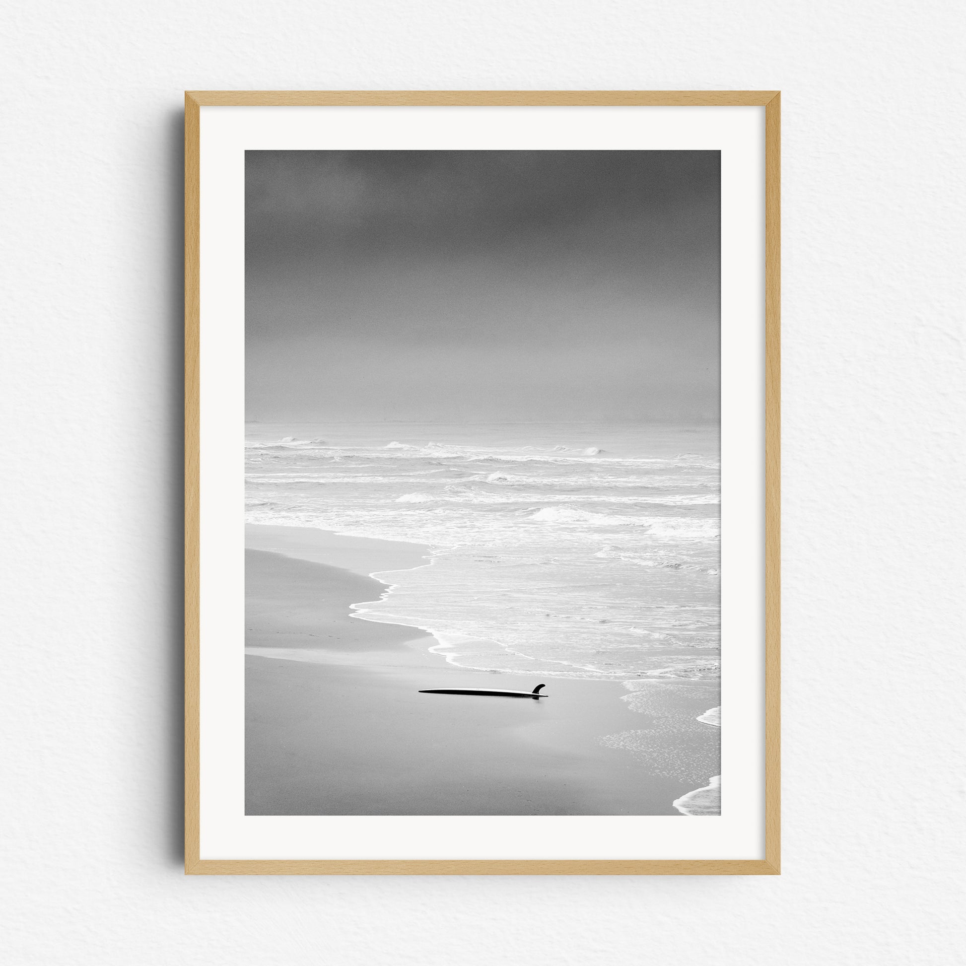 Surfboard lying in the sand on a deserted Dutch beach, framed in natural wood, capturing calm and moody surf photography from The Netherlands. Captured by Jop Hermans