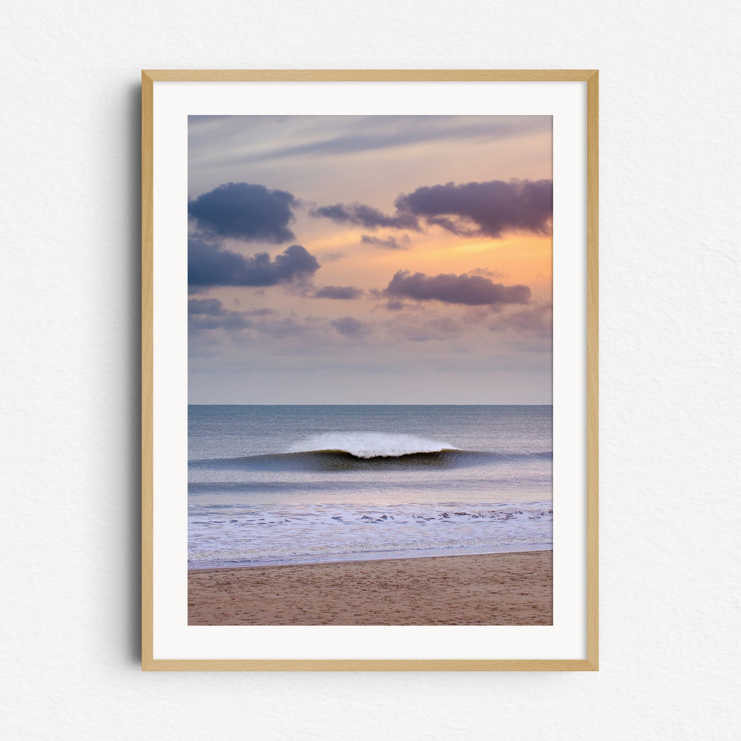 A glowing orange sky lights up a breaking North Sea wave with dramatic spray. Framed in natural wood for a warm touch.