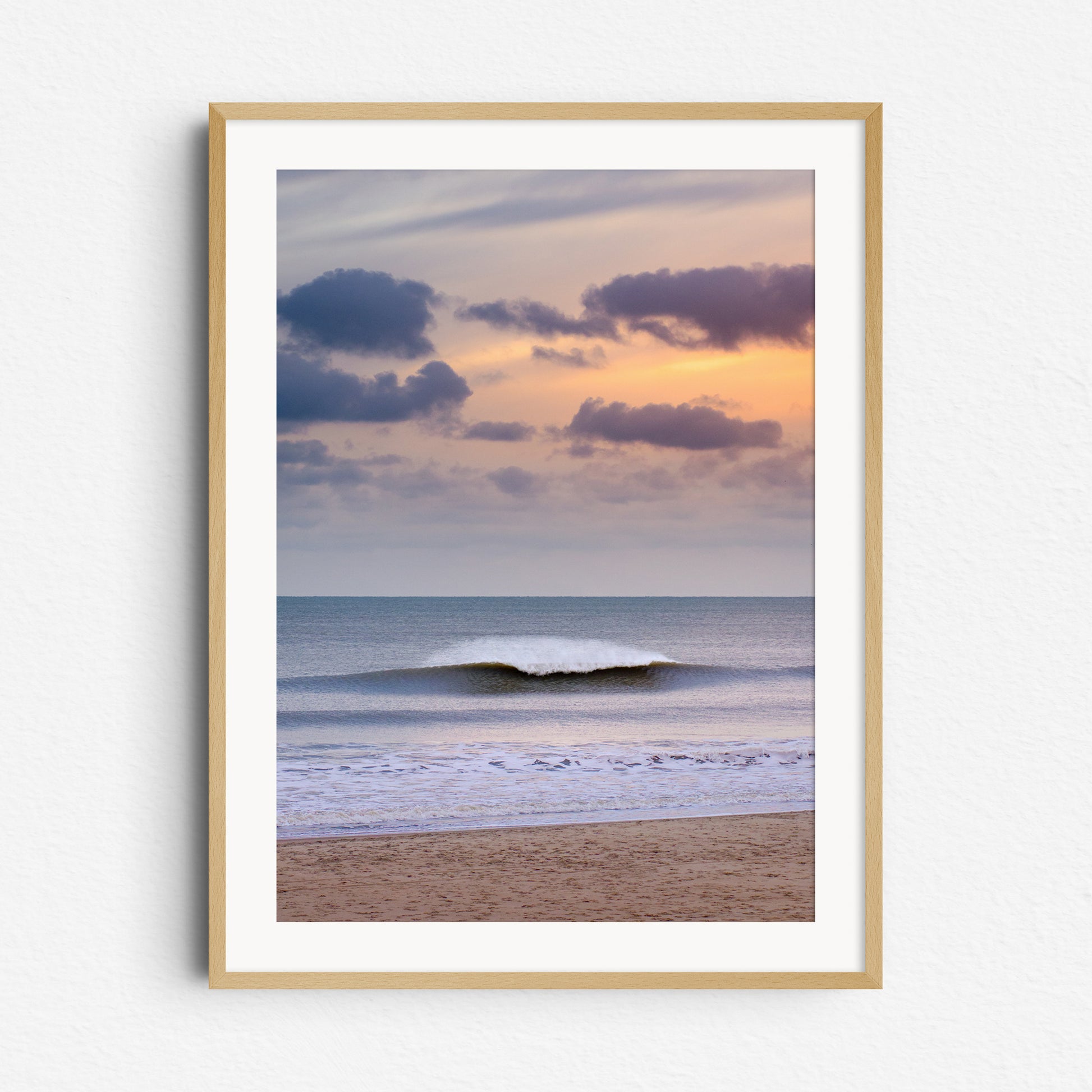 A glowing orange sky lights up a breaking North Sea wave with dramatic spray. Framed in natural wood for a warm touch.