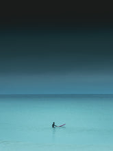 Load image into Gallery viewer, Turquoise coloured sea water with one surfer sitting on a ping surfboard. A photograph with a dark and serene mood. Photo art captured in The Hague.
