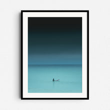 Load image into Gallery viewer, Turquoise photo of a surfer in the North Sea, sitting on a board, framed in black wood. Photo art on the wall for ocean enthusiasts.
