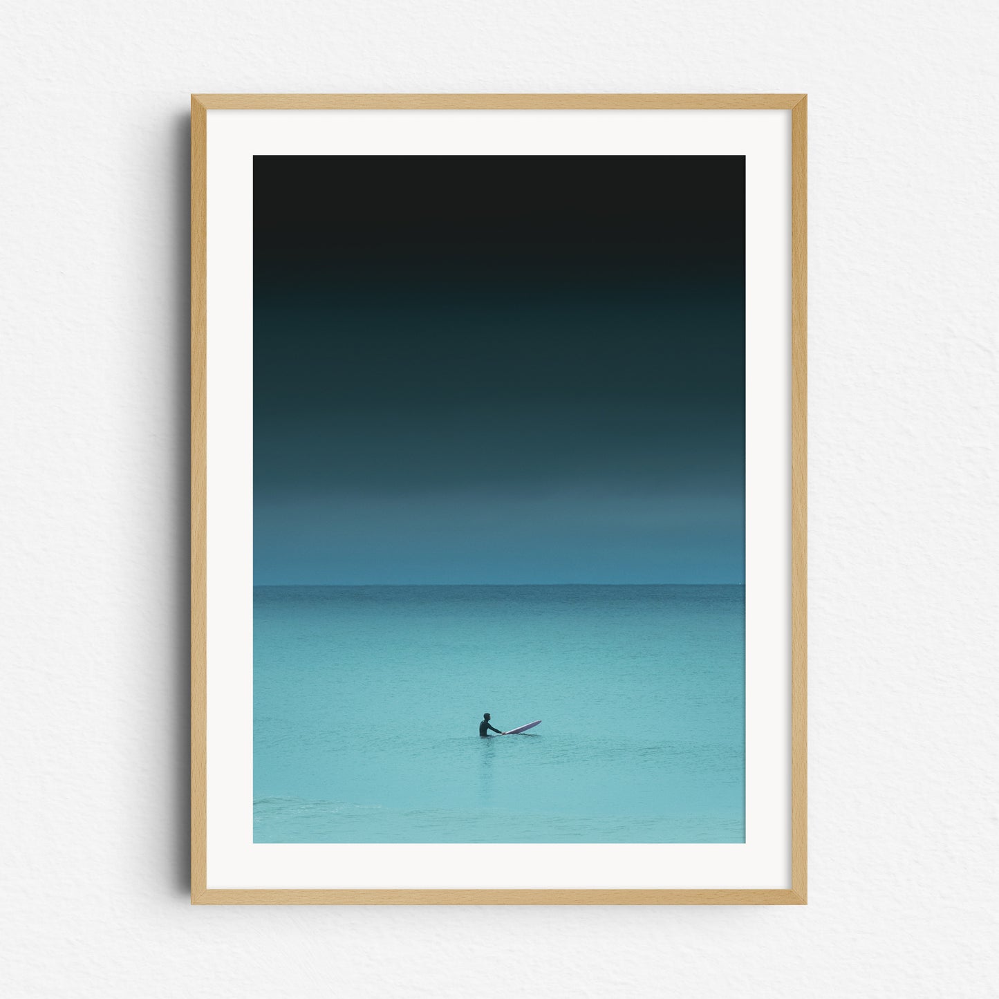 Moody turquoise nature photography of a surfer in the North Sea waiting for a wave. Framed in natural wood, ideal for nature and surf photography lovers. Captured by Jop Hermans