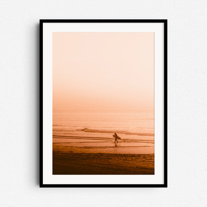 A framed photo poster of a surfer and beach scene with an orange sunset glow, captured in Scheveningen, framed in black wood for a dramatic and peaceful display.