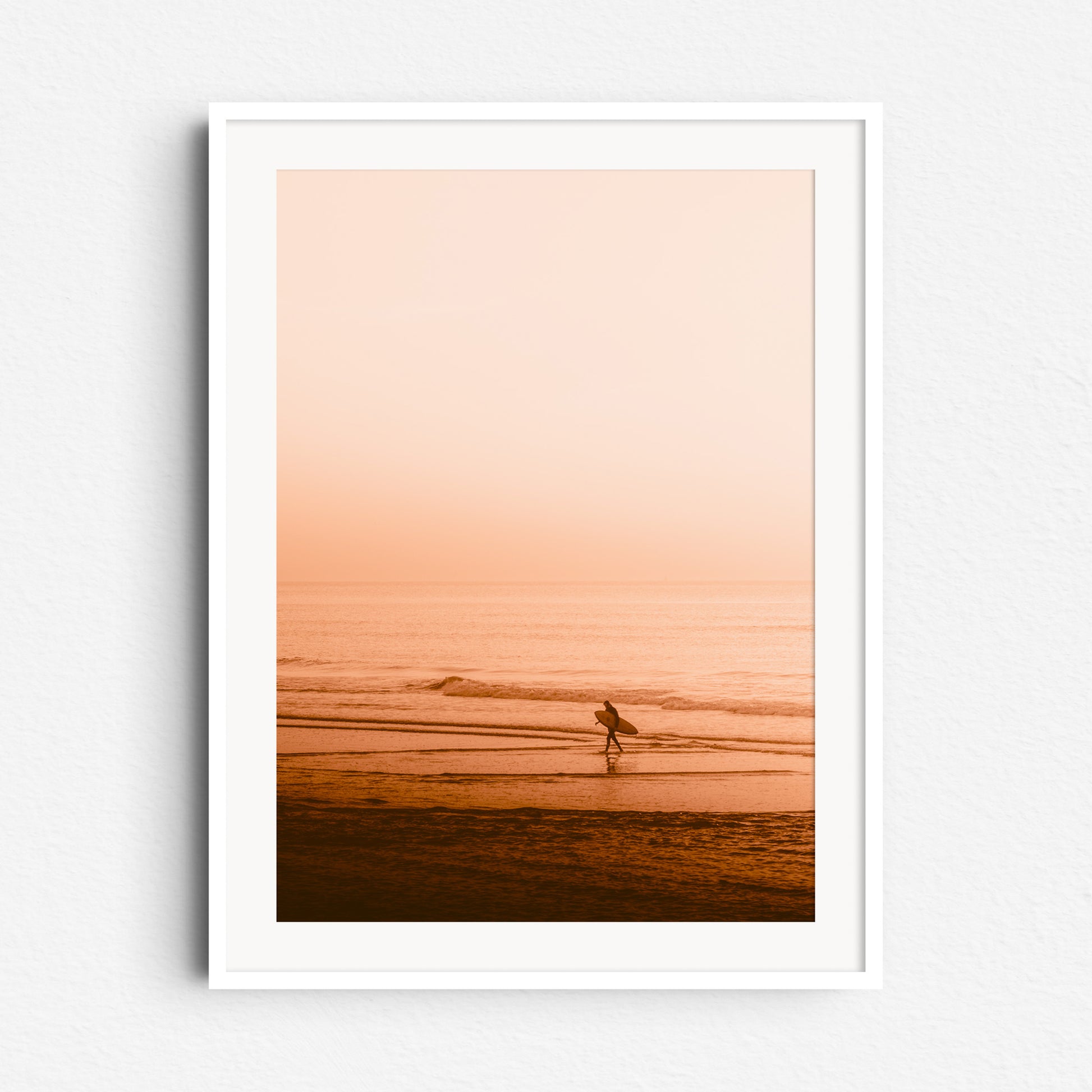 A surder walks in a serene Scheveningen sunset beach scene. Photo print framed in white wood, perfect for calming wall decoration.